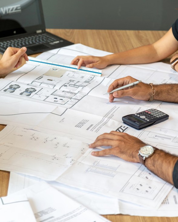 people sitting around table with laptop, calculator multiple blueprint papers